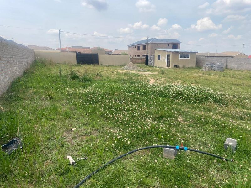 A vacant residential plot featuring a perimeter wall, an existing outbuilding, and open grass area, suitable for future development.