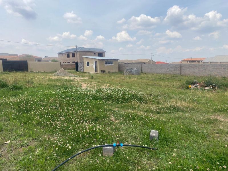 A vacant residential plot featuring a small outbuilding, perimeter walling, and established grass, offering potential for future development.