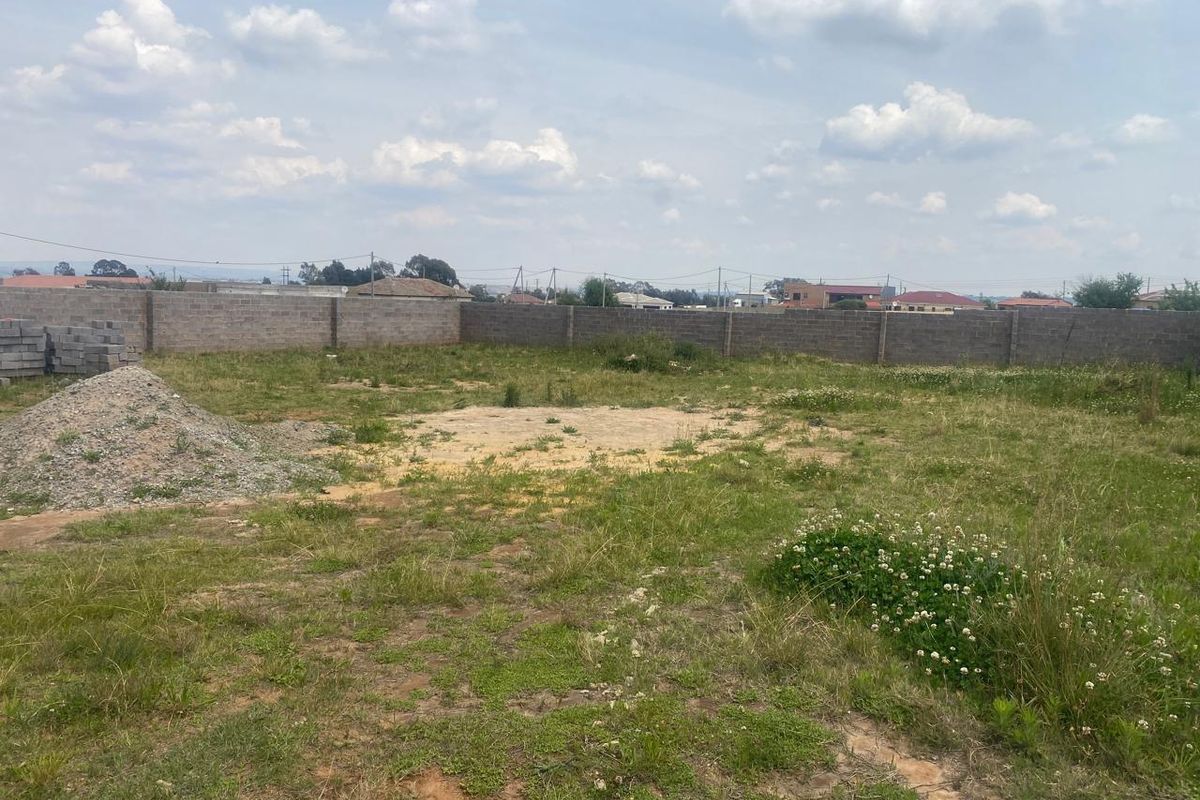 A vacant residential plot featuring a perimeter boundary wall and open, undeveloped land.