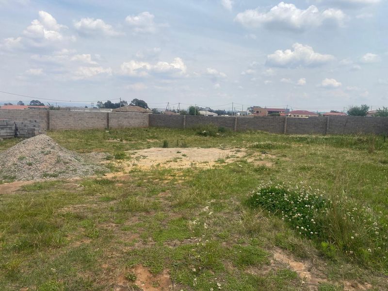 A vacant residential plot featuring a perimeter boundary wall and open, undeveloped land.