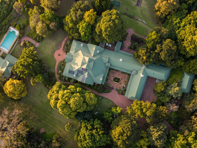 An expansive aerial view of a large residential property featuring a sprawling home with a metal roof, solar panels, swimming pool, and tennis court.