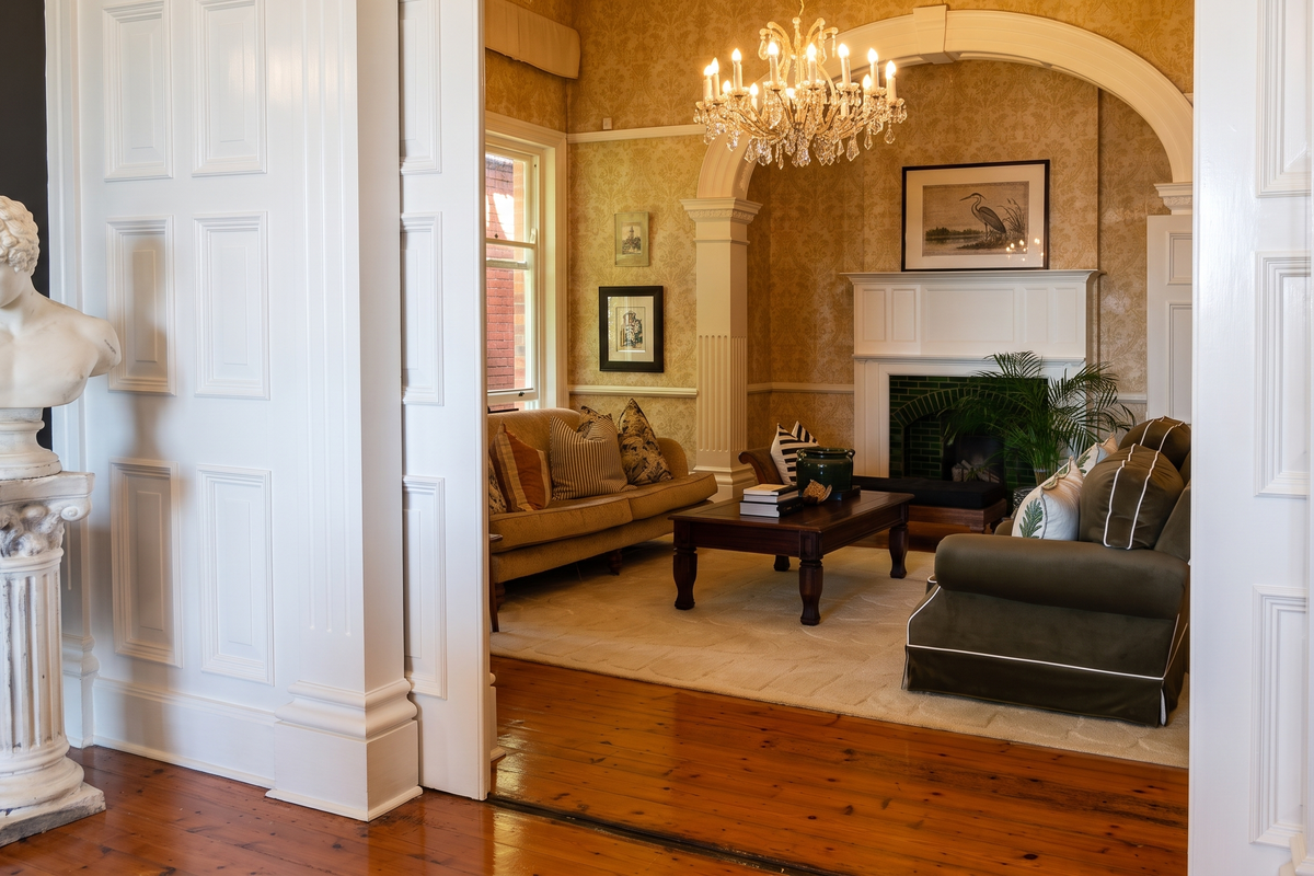 Elegant living room featuring a fireplace with tiled surround, classic archway, decorative columns, polished timber flooring, and a sophisticated chandelier.