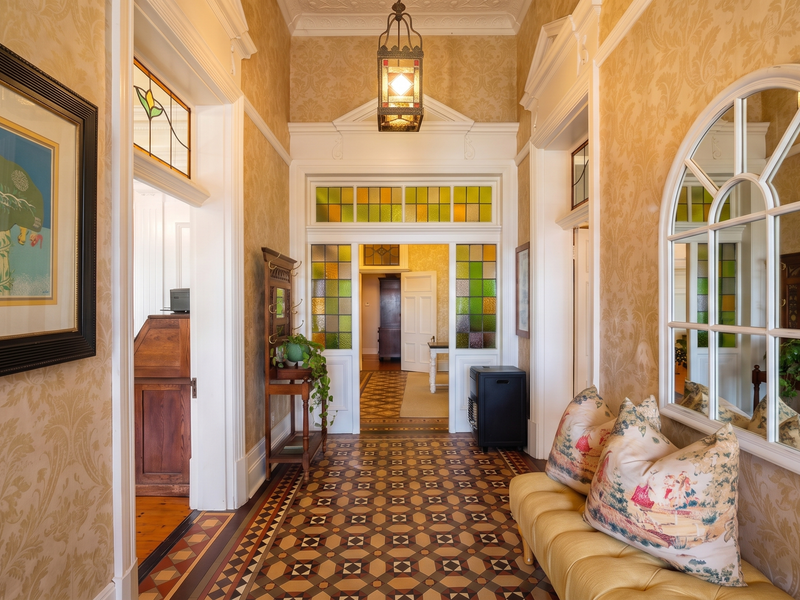 A beautifully preserved period hallway featuring intricate encaustic floor tiles, stained glass transom windows, and elegant architectural detailing throughout.