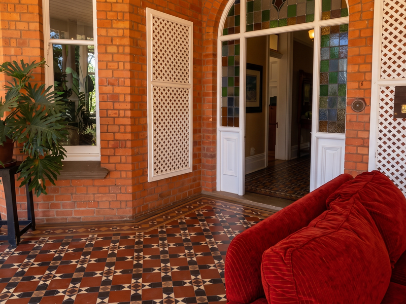 A charming covered patio featuring classic exposed brick walls, intricate patterned tile flooring, and a beautiful arched entrance with stained glass detailing.