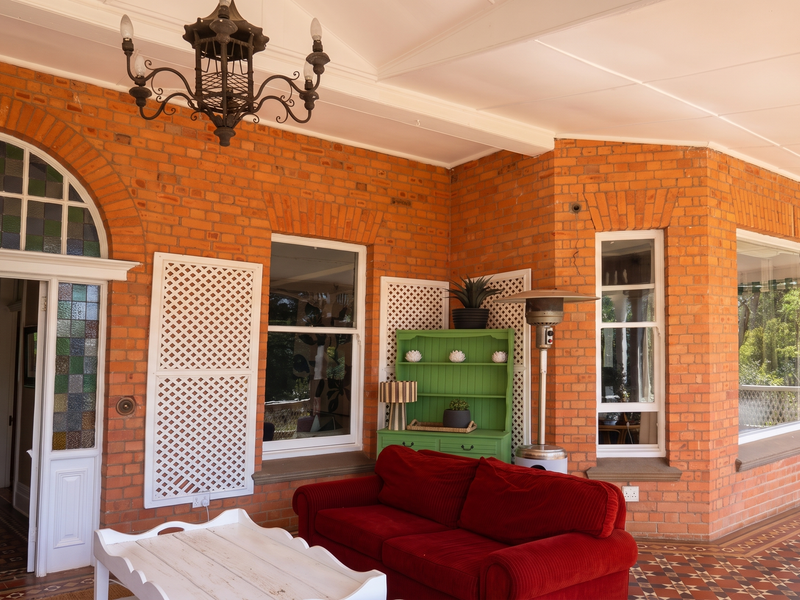 A spacious covered patio featuring exposed brick walls, vaulted ceilings, a decorative wrought iron chandelier, and classic patterned tiled flooring.