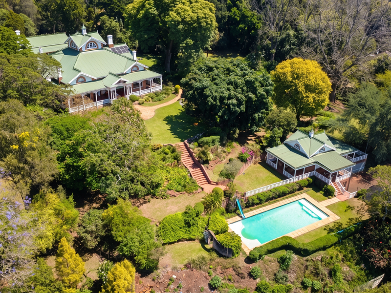 Aerial view of a large estate featuring a main residence, secondary dwelling, swimming pool, tennis court, and extensive landscaped gardens.