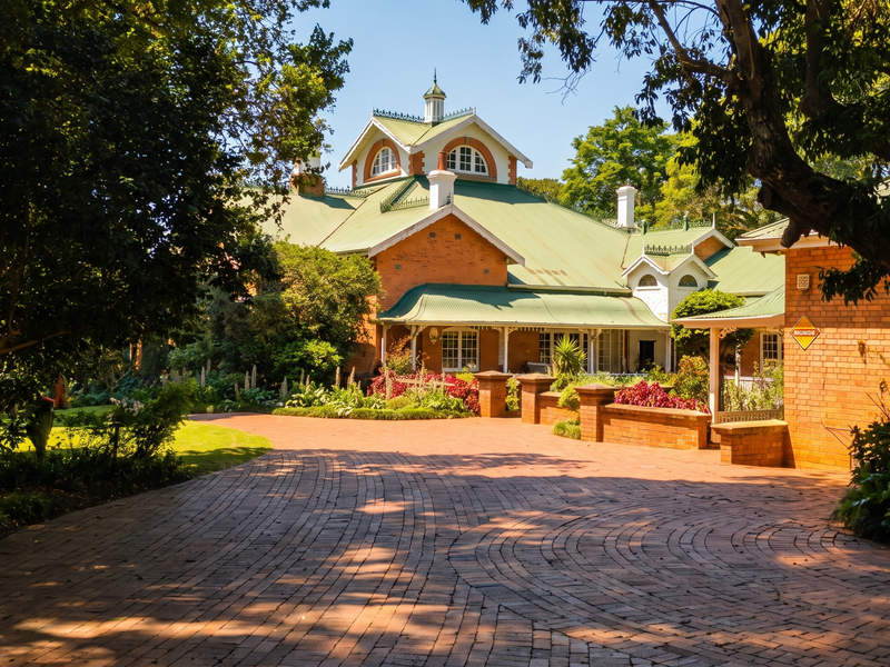 A beautiful, well-maintained brick residence featuring a sweeping brick driveway, established gardens, and a classic metal roof with a covered veranda.