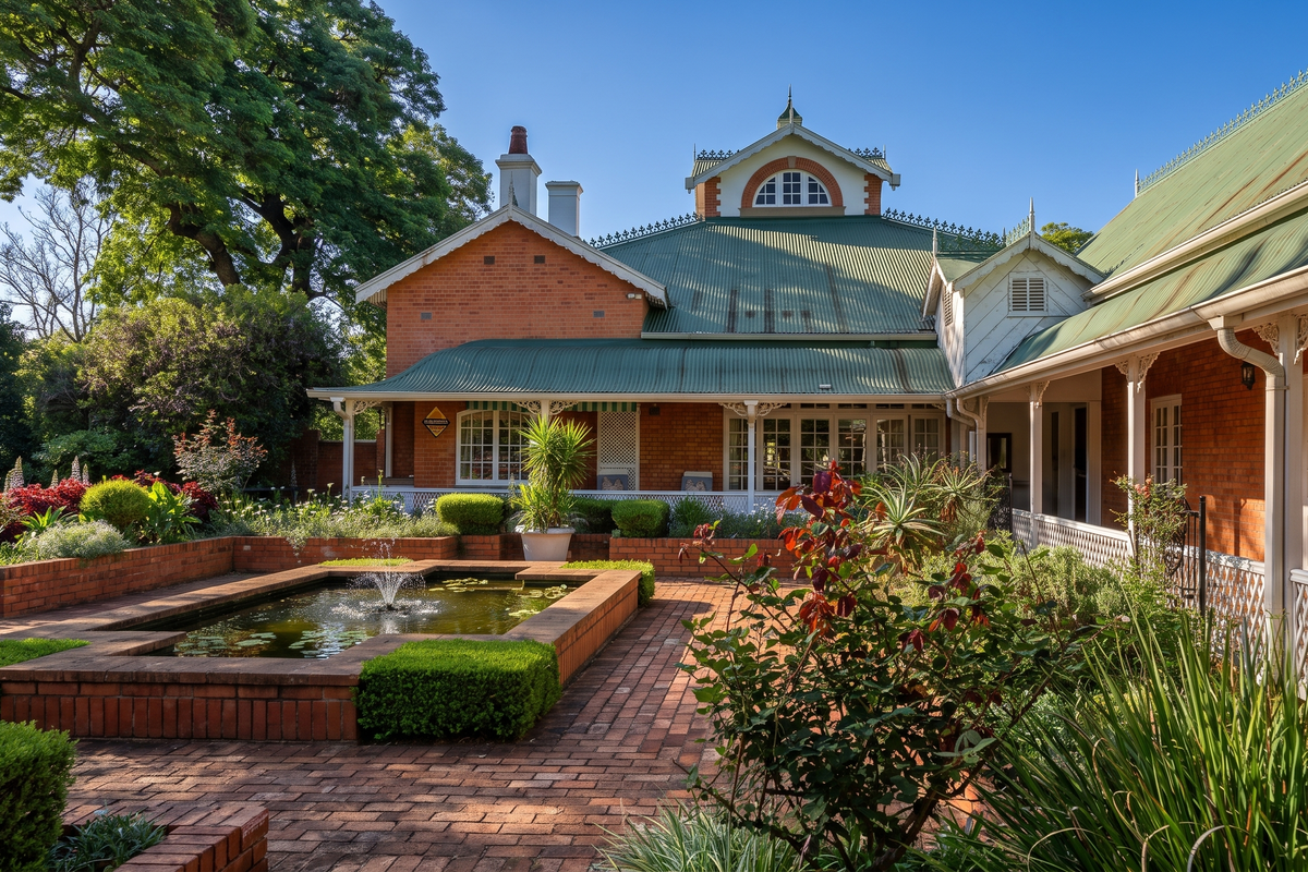 A beautifully maintained rear garden featuring a brick-paved courtyard, a central water feature, and a classic brick home with a covered veranda.