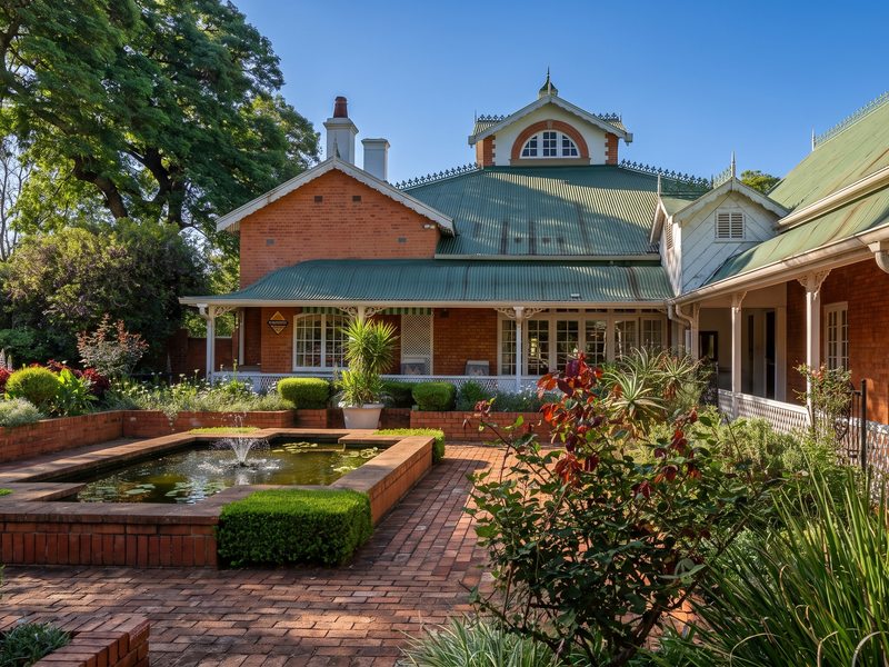 A beautifully maintained rear garden featuring a brick-paved courtyard, a central water feature, and a classic brick home with a covered veranda.