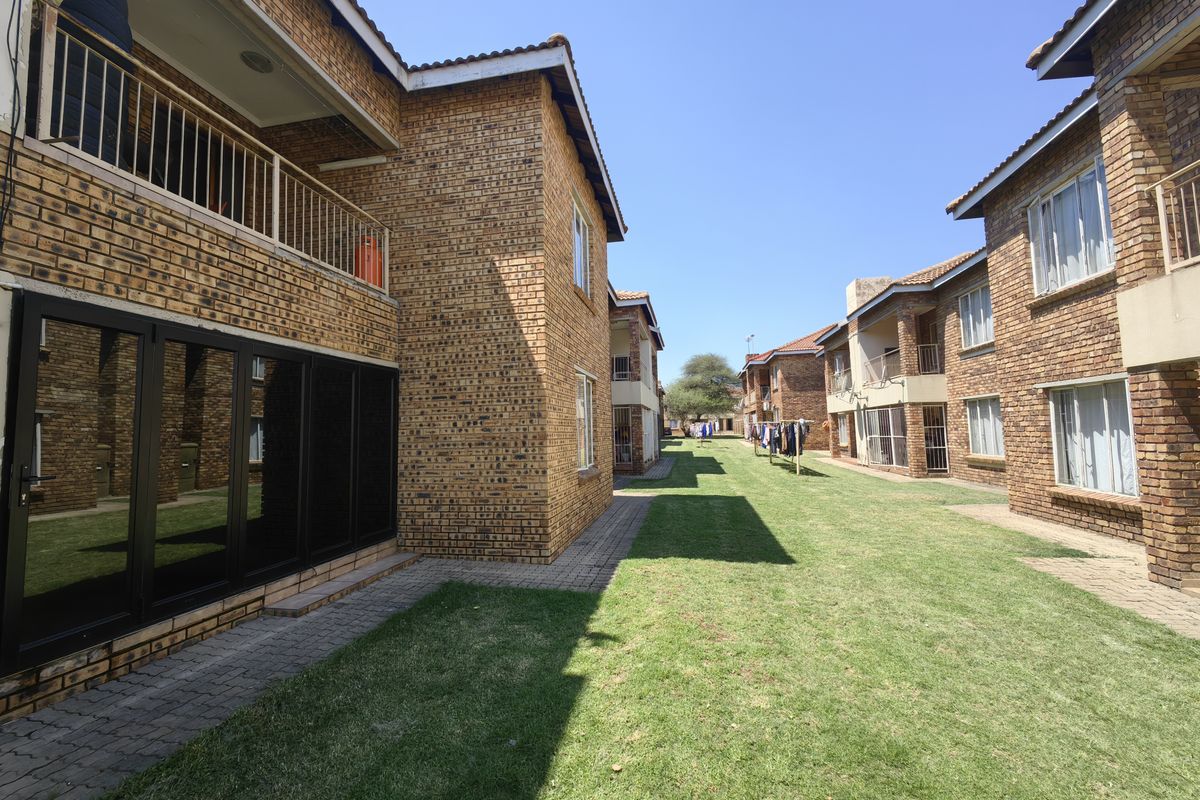A view of the rear exterior of the apartment complex, featuring face brick buildings, manicured lawns, paved walkways, and private balconies.