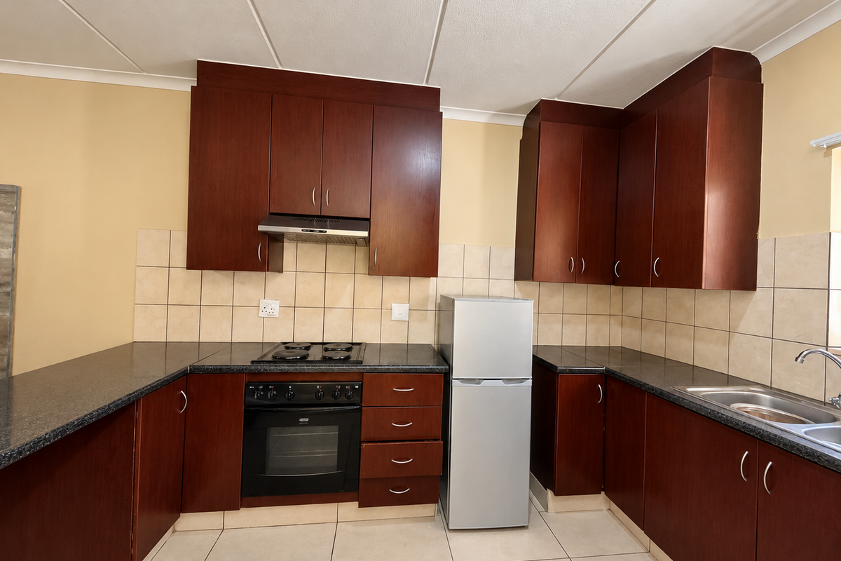 A functional kitchen featuring dark wood cabinetry, granite countertops, built-in oven, electric hob, and a stainless steel sink with tiled backsplash.