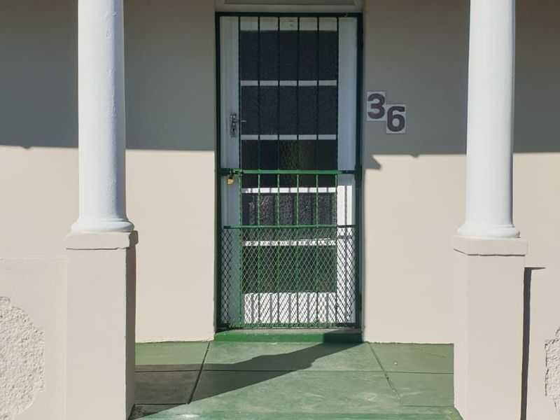 Front entrance of the house featuring concrete steps, decorative columns, and a security gate.