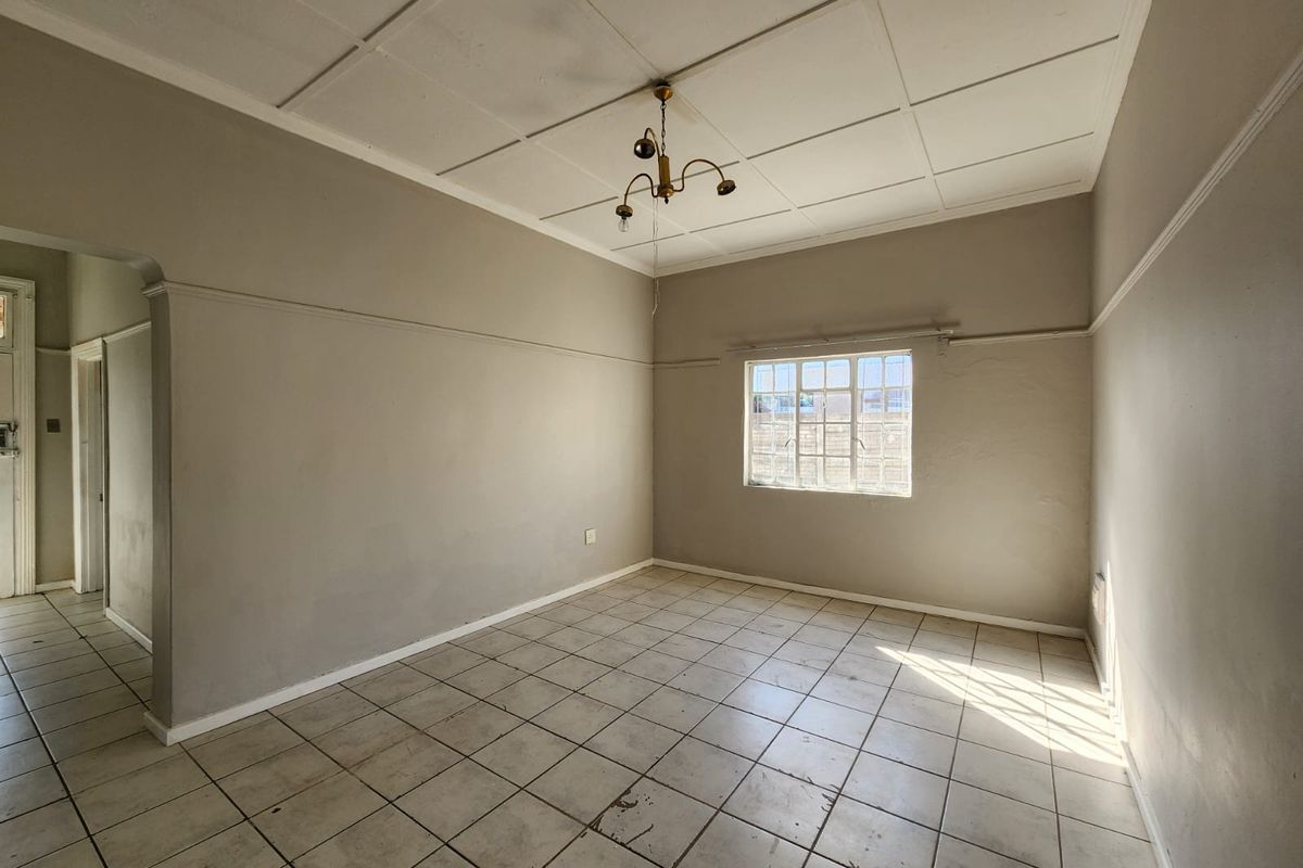 An empty living room featuring tiled flooring, a ceiling tile finish, and a steel-framed window, offering a blank canvas for renovation.