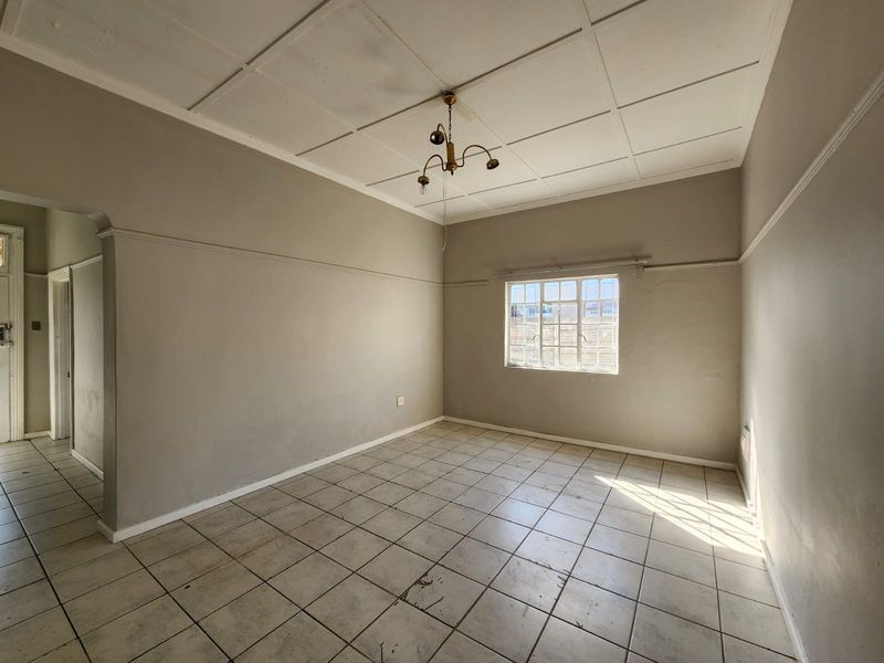 An empty living room featuring tiled flooring, a ceiling tile finish, and a steel-framed window, offering a blank canvas for renovation.