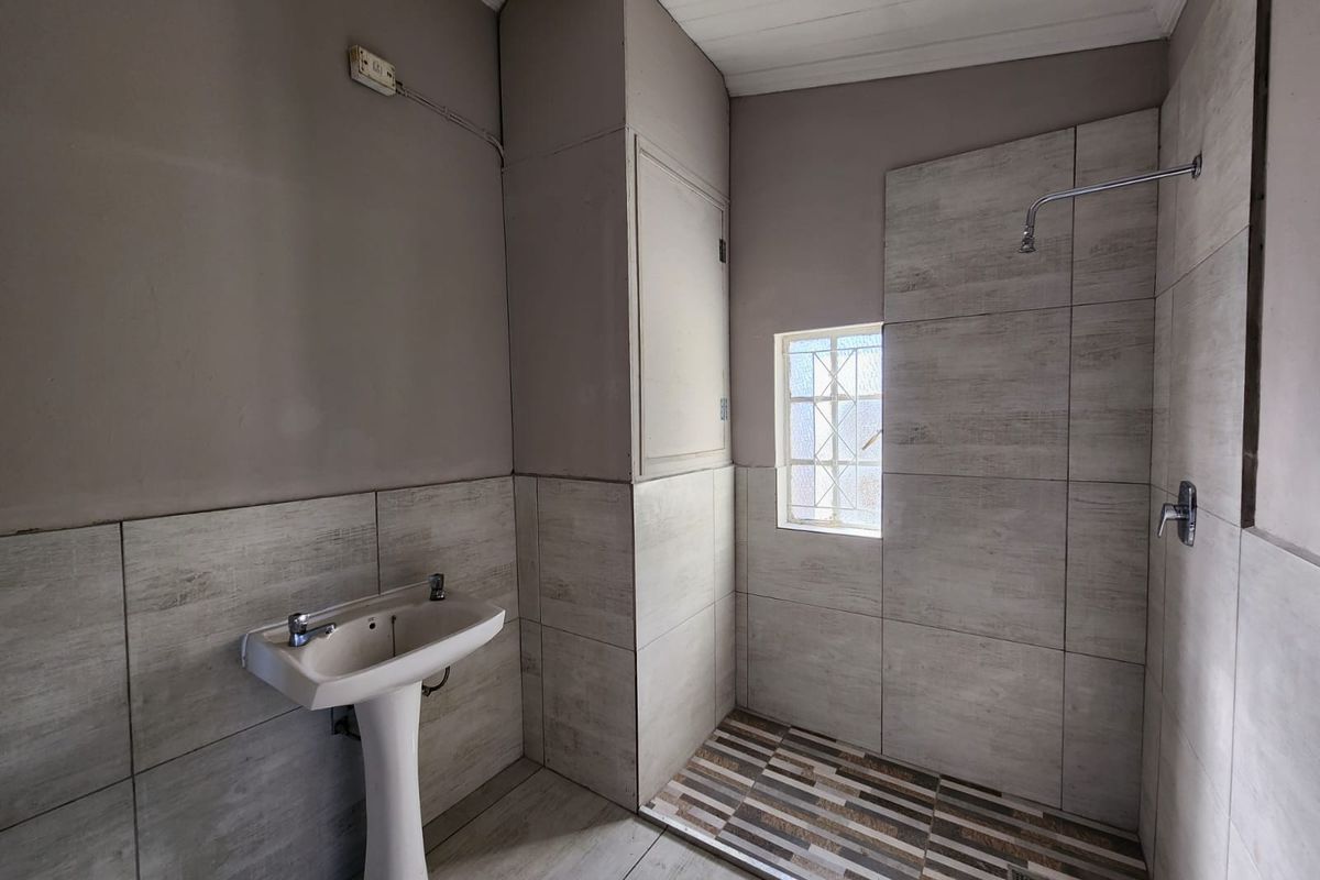 A functional bathroom featuring a pedestal washbasin and a walk-in shower with modern grey-toned wall and floor tiling.