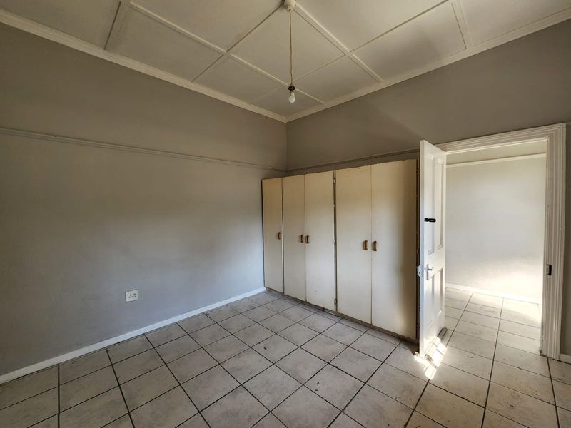 An empty bedroom featuring tiled flooring, a panelled ceiling, and built-in cupboards, offering a blank canvas for renovation and interior design updates.