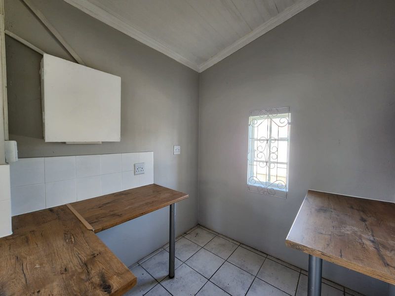 A functional scullery or utility area featuring tiled flooring, laminate countertops, and a window with security bars.