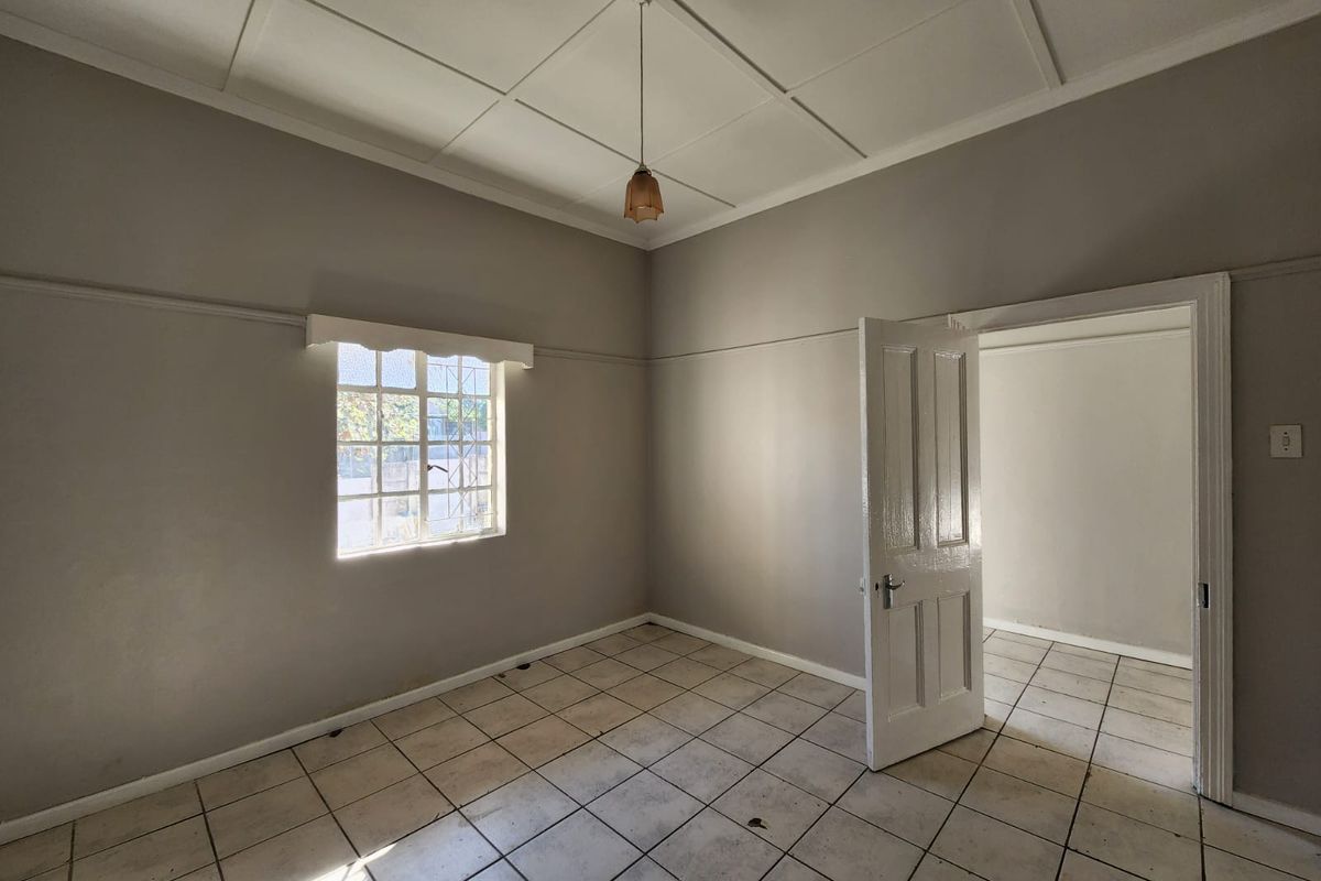 An empty bedroom featuring tiled flooring, a panelled ceiling, and a classic timber door, offering a blank canvas for renovation or interior design.