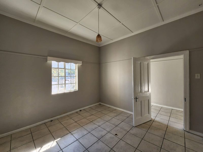 An empty bedroom featuring tiled flooring, a panelled ceiling, and a classic timber door, offering a blank canvas for renovation or interior design.