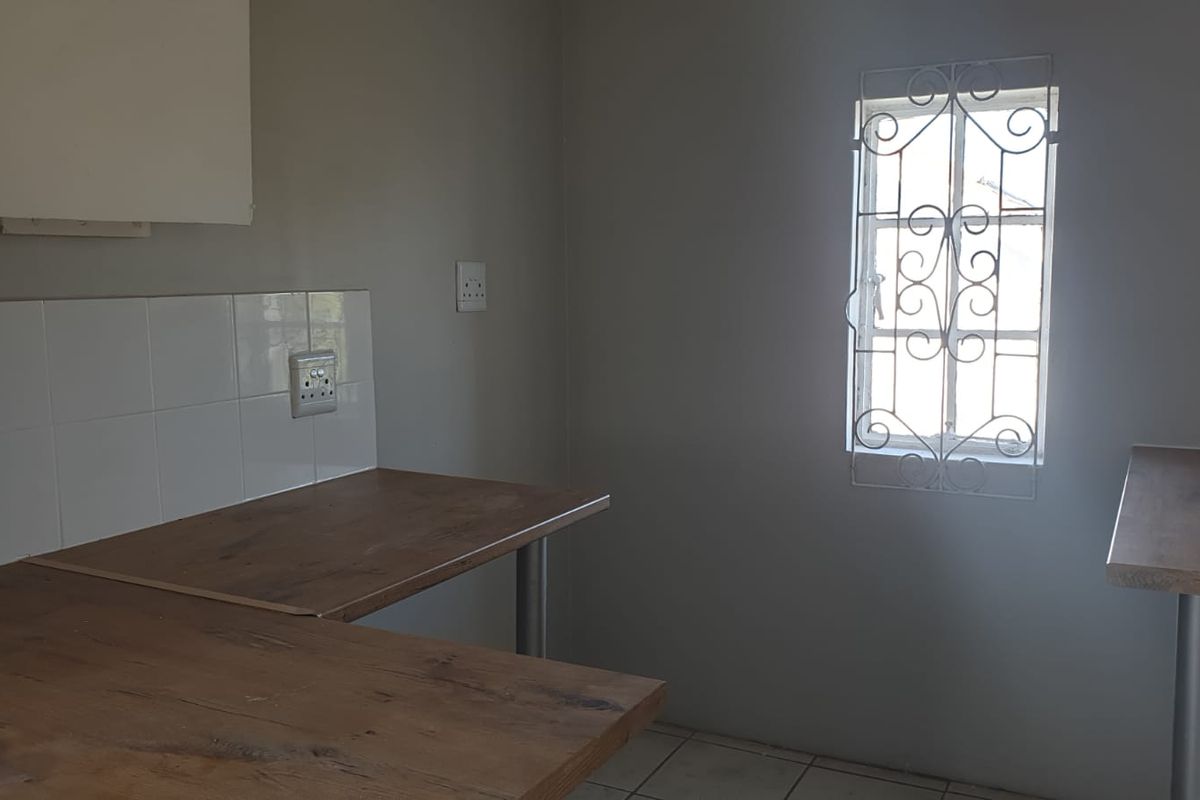 A functional kitchen area featuring laminate countertops, tiled splashbacks, and a window with a security gate, offering a clean and practical workspace.