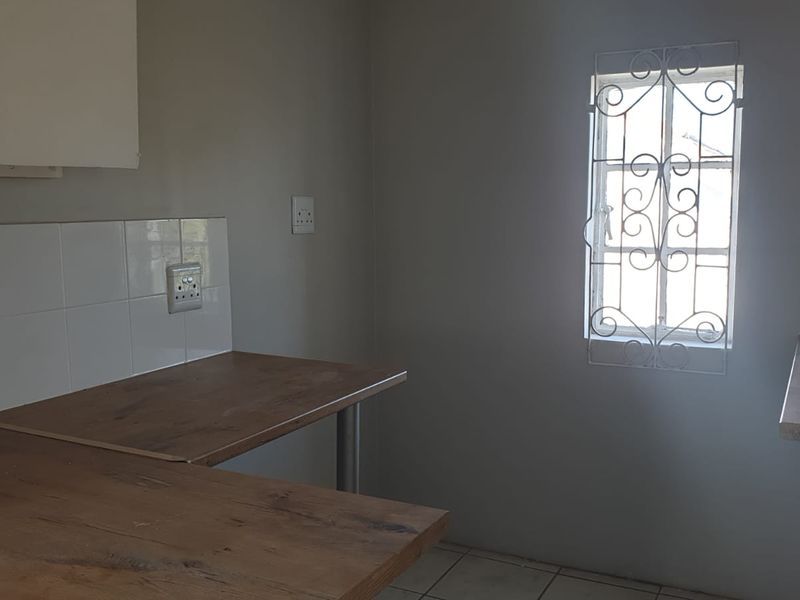 A functional kitchen area featuring laminate countertops, tiled splashbacks, and a window with a security gate, offering a clean and practical workspace.