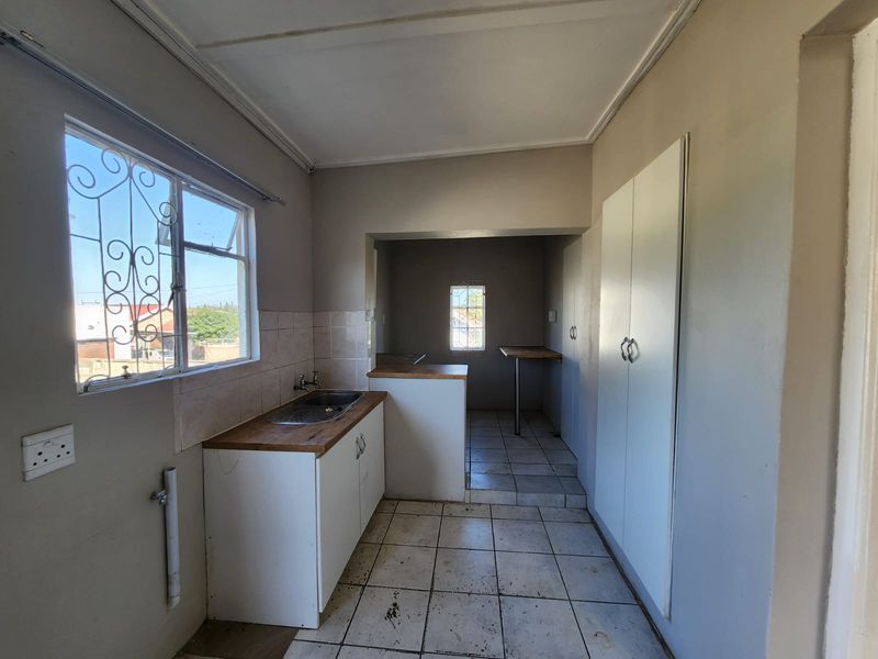 A functional kitchen space featuring built-in cabinetry, a stainless steel sink, tiled flooring, and ample storage cupboards, ready for a modern update.