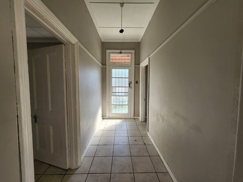 A vacant hallway featuring tiled flooring, classic panelled doors, and a glass-panelled entrance door with a transom window, requiring cosmetic updates.