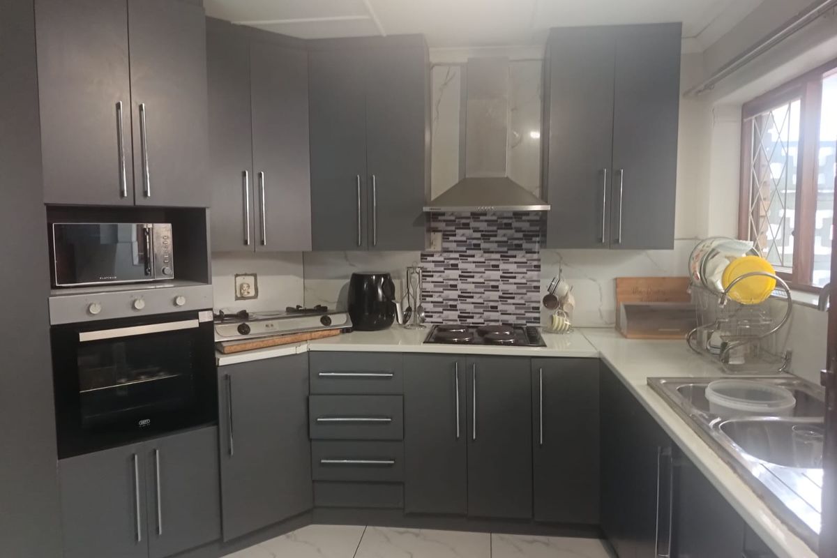 Modern kitchen featuring dark grey cabinetry, built-in oven and microwave, gas hob with extractor fan, and tiled flooring.
