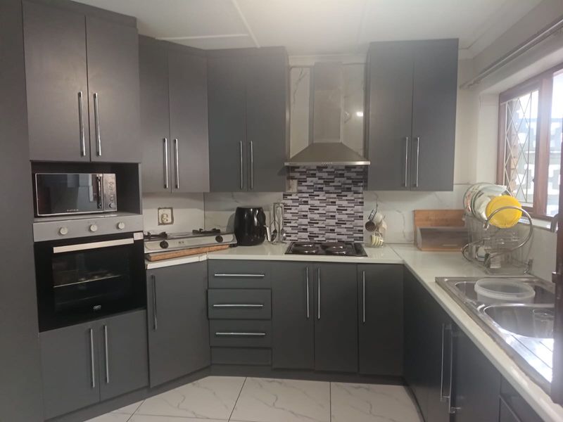Modern kitchen featuring dark grey cabinetry, built-in oven and microwave, gas hob with extractor fan, and tiled flooring.