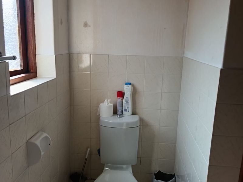 A compact bathroom featuring a standard toilet, tiled walls, and tiled flooring, currently requiring cosmetic updates to the wall finishes.