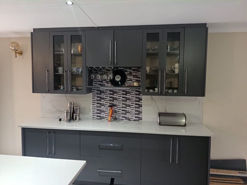 Modern kitchen featuring dark grey cabinetry, white stone countertops, and a stylish mosaic tile backsplash with integrated glass-fronted display cabinets.