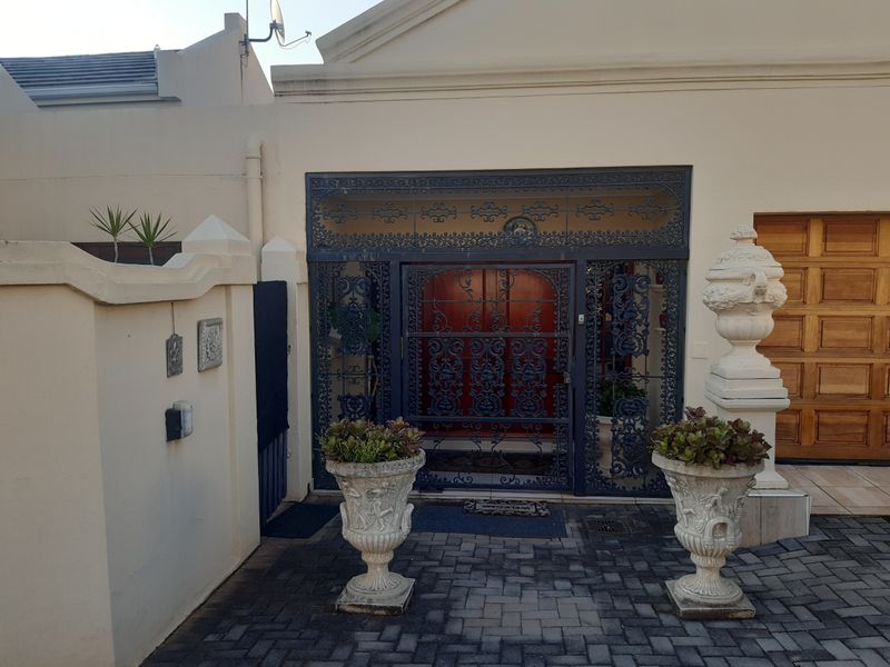Front entrance of the duet property featuring a decorative wrought iron security gate, paved driveway, and integrated wooden garage door.