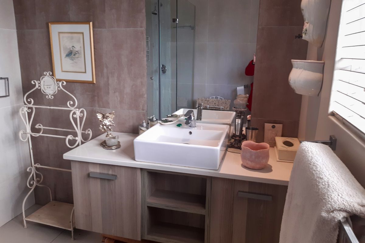 Modern bathroom featuring a vanity cabinet with a countertop basin, large wall mirror, and a glass-enclosed shower with neutral wall tiling.