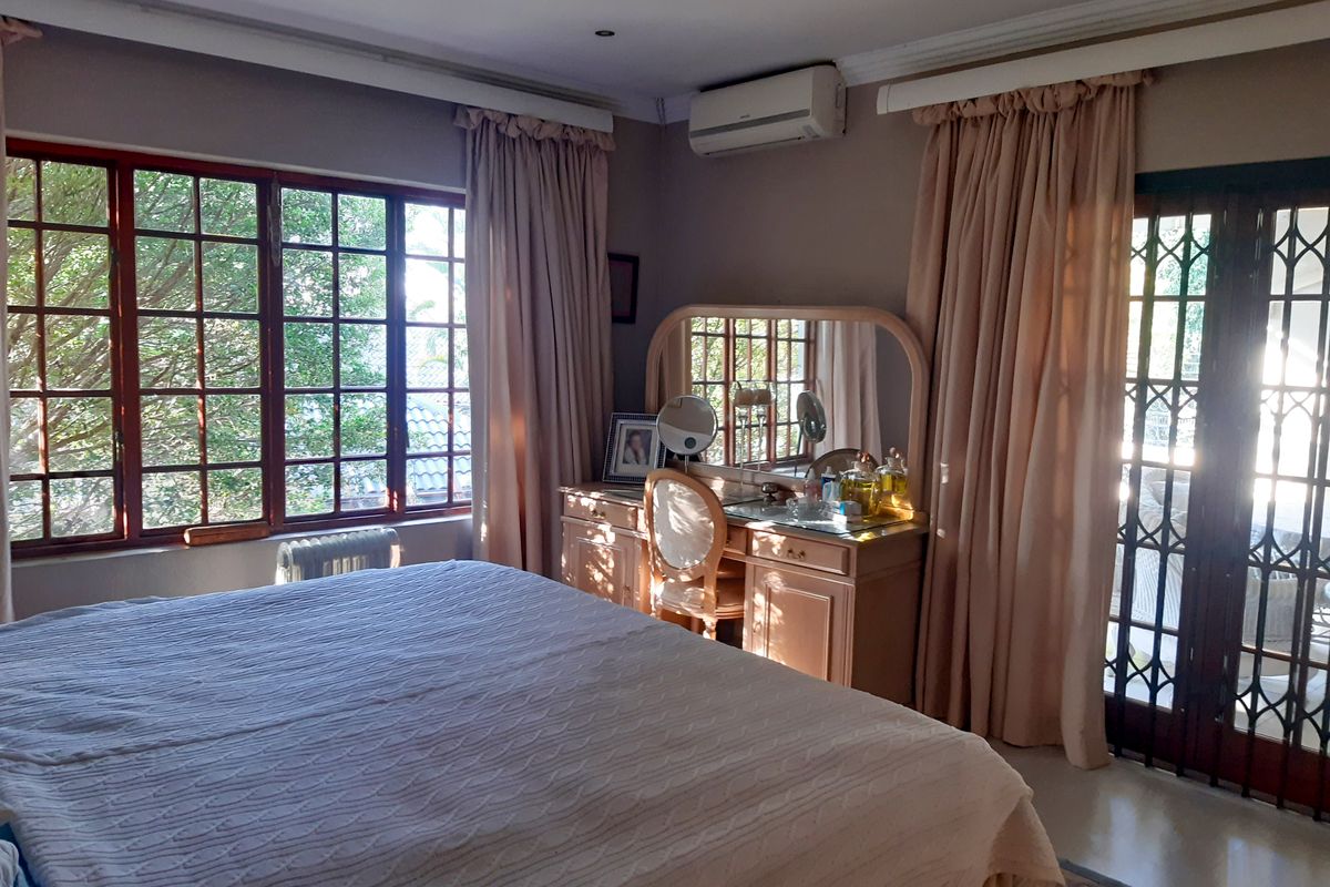 A well-lit bedroom featuring tiled flooring, an air conditioning unit, and large windows with access to an outdoor area through french doors.