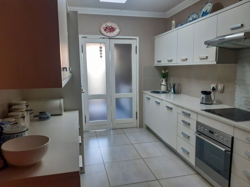 A functional kitchen featuring white cabinetry, stone countertops, integrated oven and hob, and tiled flooring with direct access to an outdoor area.