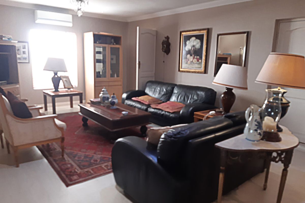 A spacious living room featuring tiled flooring, cove cornicing, and a wall-mounted air conditioning unit, offering a comfortable and functional living space.