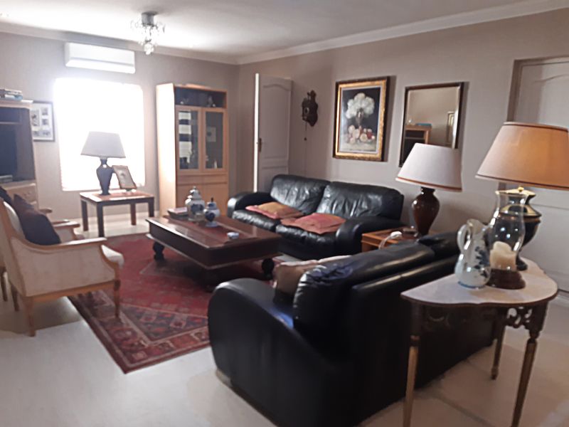 A spacious living room featuring tiled flooring, cove cornicing, and a wall-mounted air conditioning unit, offering a comfortable and functional living space.