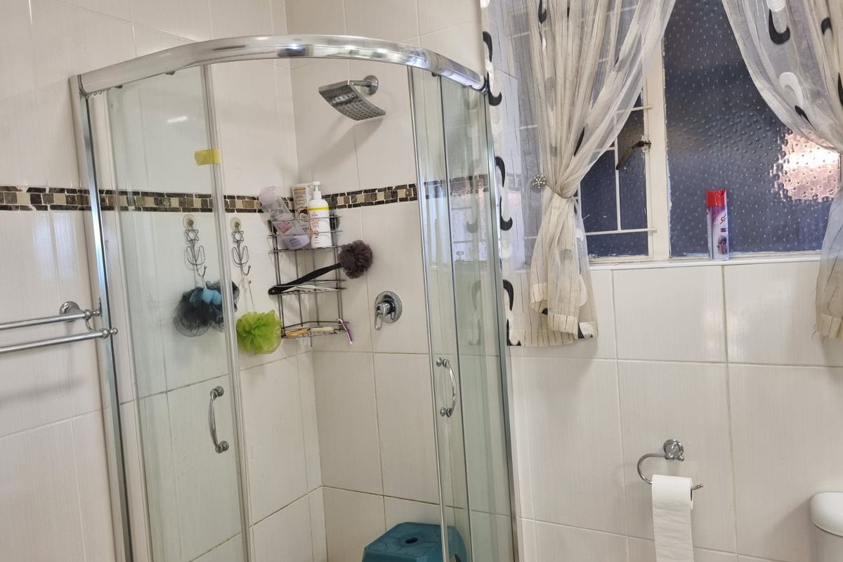 A functional bathroom featuring a curved glass shower enclosure, tiled walls, and a window with security bars.