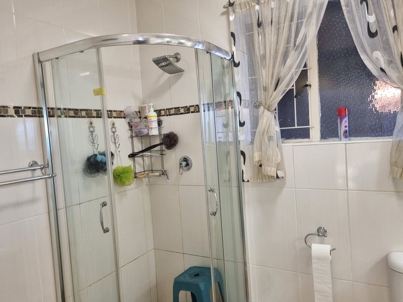 A functional bathroom featuring a curved glass shower enclosure, tiled walls, and a window with security bars.