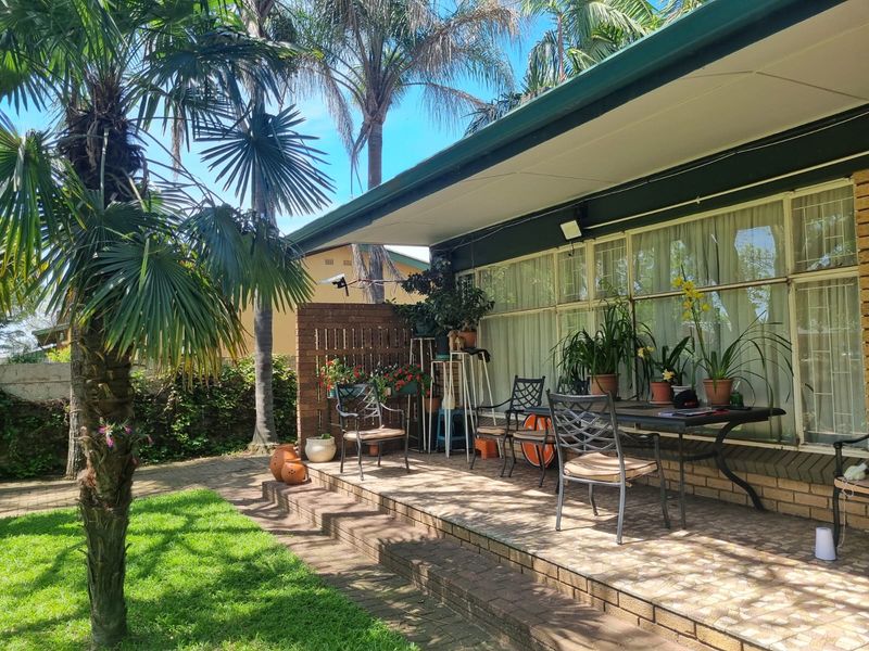A covered outdoor patio area featuring brick paving and a brick privacy screen, providing direct access to the garden through large glass sliding doors.