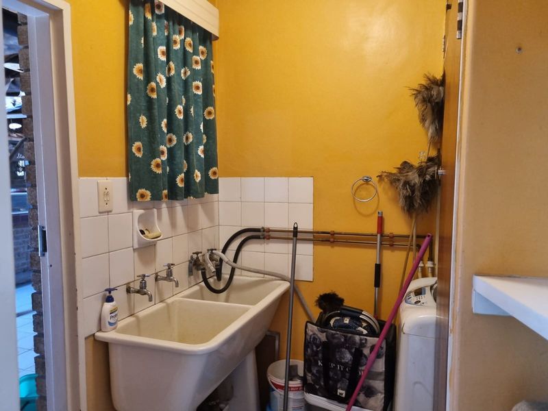 A functional laundry area featuring a double ceramic sink, exposed copper plumbing, and tiled splashback, offering potential for modernization and improved utility storage.