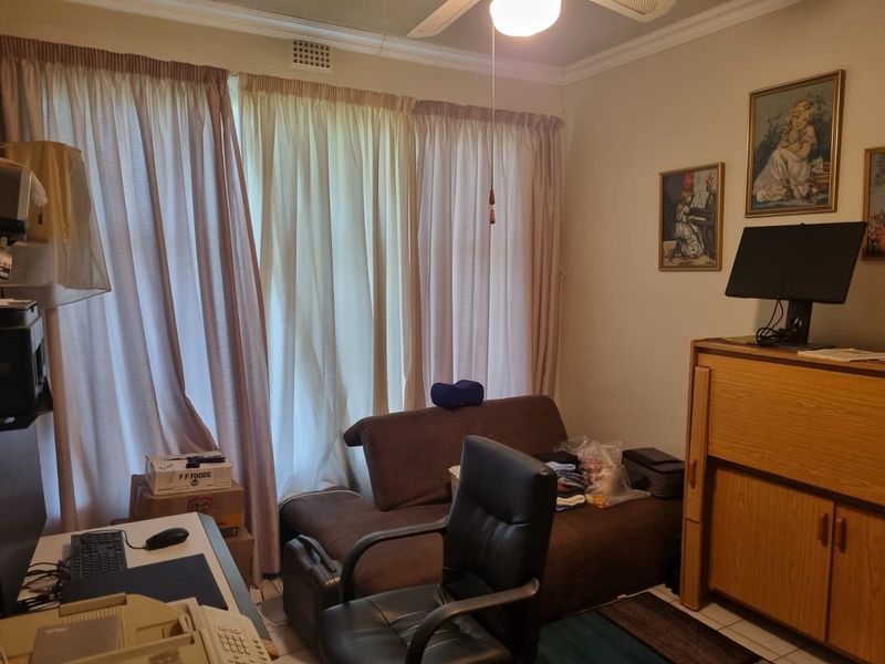 A functional bedroom space featuring tiled flooring, a ceiling fan, and large window curtains, offering a neutral base for potential interior updates.
