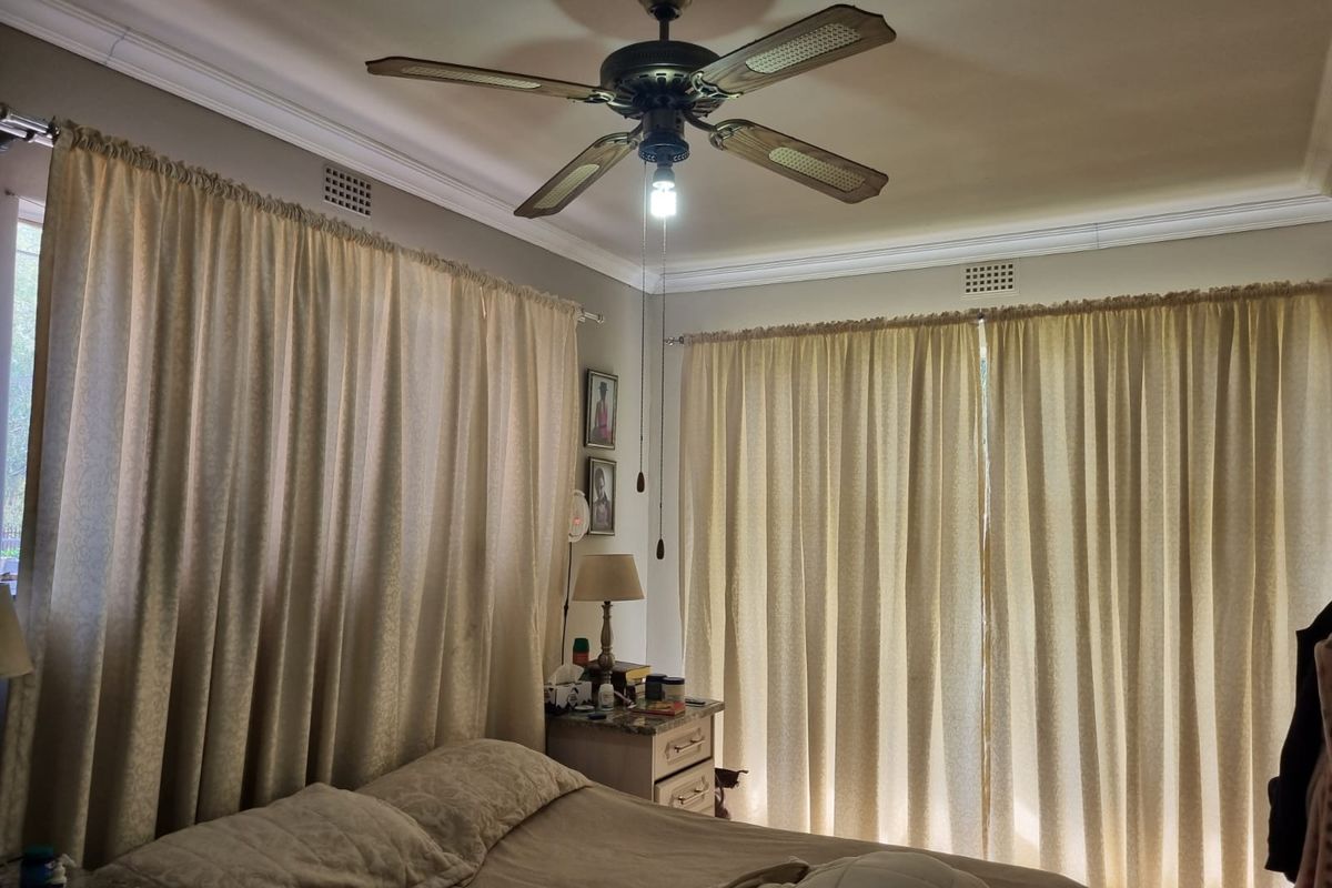 A bedroom featuring crown molding, a ceiling fan, and large windows covered by curtains.