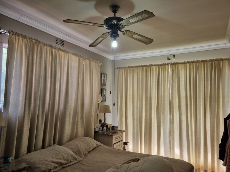 A bedroom featuring crown molding, a ceiling fan, and large windows covered by curtains.