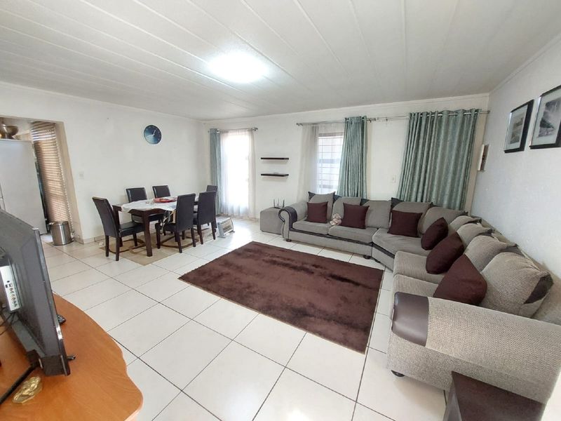 Spacious open-plan living and dining area featuring neutral tiled flooring and large windows with curtain rails.