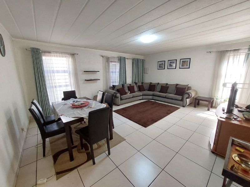 Spacious open-plan living and dining area featuring neutral tiled flooring and a panelled ceiling, offering a versatile layout for comfortable family living.