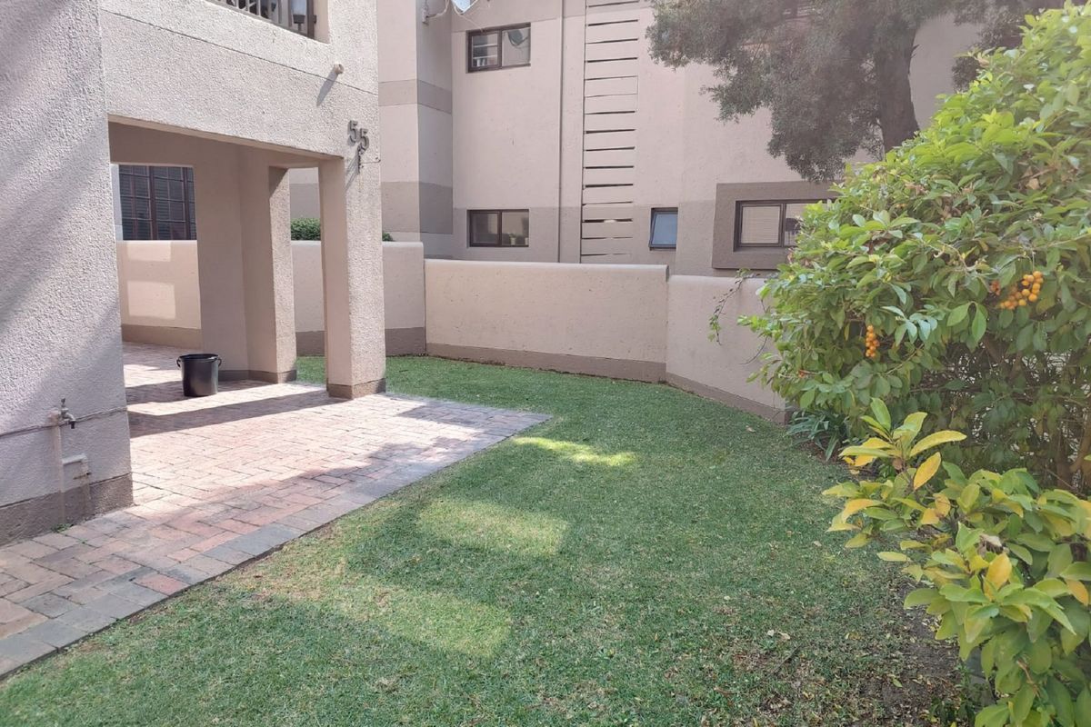 A private rear garden area featuring a paved patio, well-maintained lawn, and boundary wall, providing a functional outdoor space for the apartment.