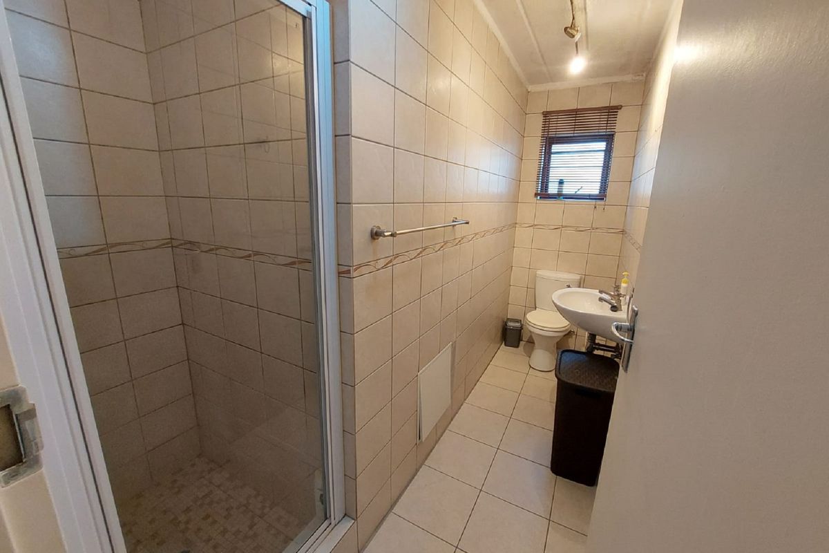 A functional bathroom featuring a shower enclosure, pedestal basin, toilet, and neutral wall and floor tiling.