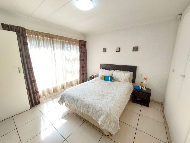A bright bedroom featuring tiled flooring, built-in cupboards, and large windows with curtain treatments.