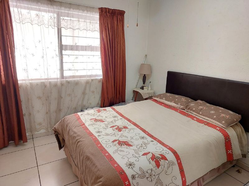 A functional bedroom featuring tiled flooring and a window equipped with security bars, providing a simple and practical living space.